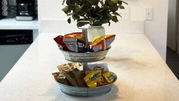 A kitchen counter with a plant, a metal bowl, and snack packets.
