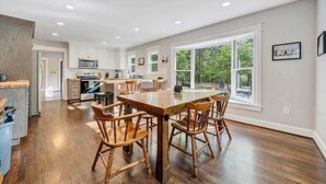 Una cocina amplia con suelo de madera, armarios blancos y una gran mesa de comedor con sillas de madera.