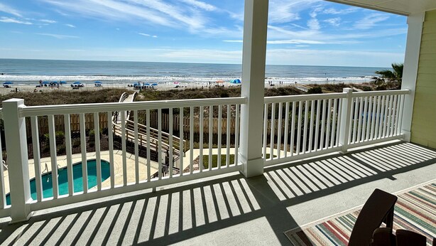Ein Balkon mit Blick auf Strand und Meer, ein Pool und ein Stuhl.