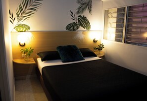 A bedroom with a bed, two bedside tables, a nightstand, a wall-mounted lamp, and a window with blinds. - Hotel Primavera Zero (Medellín)
