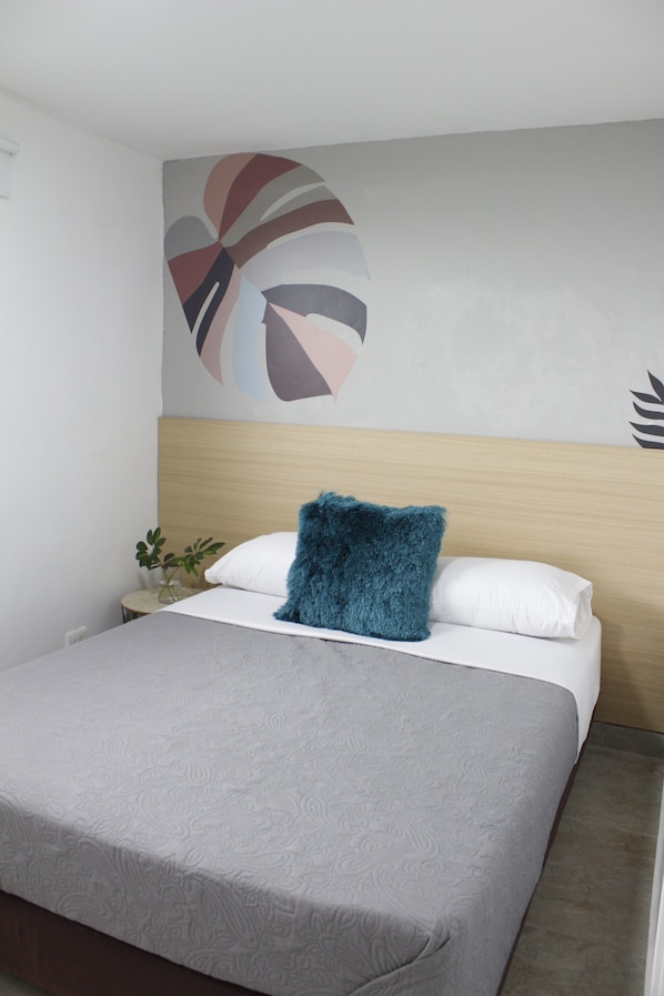 Una habitación de hotel con una cama, una mesita de noche, una planta y una pared decorada con una obra de arte geométrica.