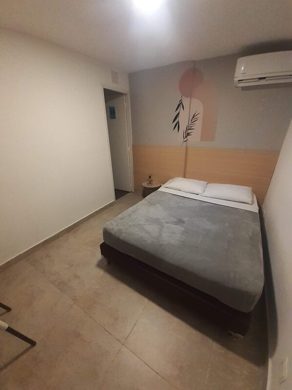 Een slaapkamer met een bed, een nachtkastje en een wandairconditioner.