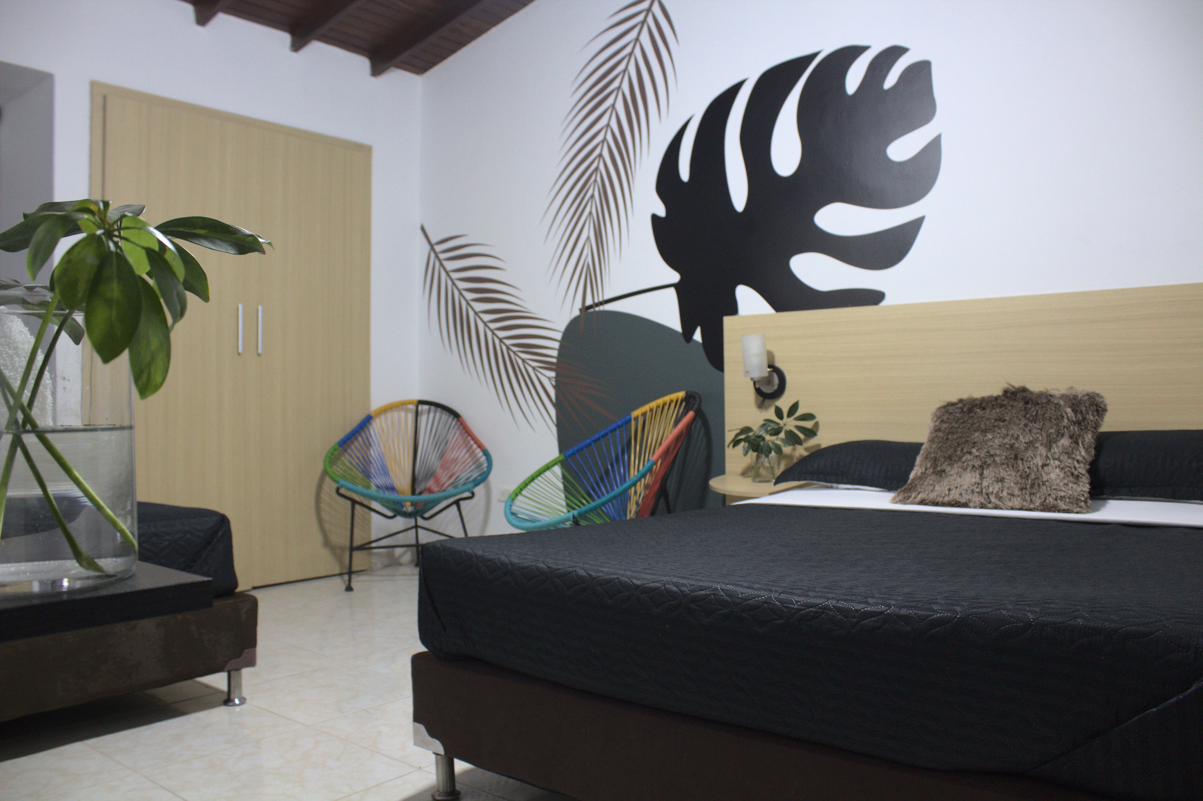 A bedroom with a bed, a chair, a plant, and a wall with a leaf design.
