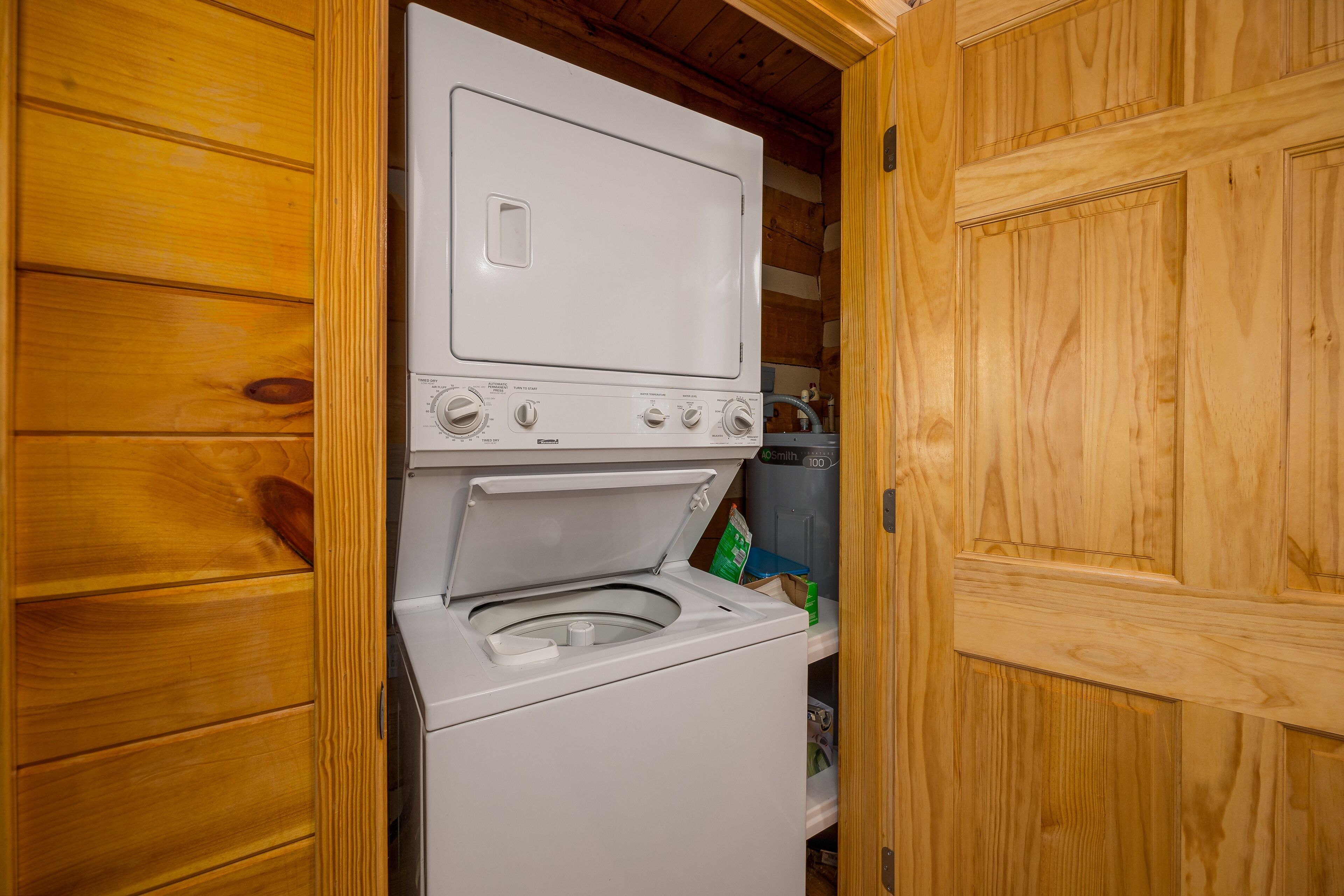 Pequeña lavandería con lavadora y secadora, paredes de madera y una puerta.