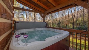 Een hottub met twee glazen wijn, omgeven door een houten terras en uitzicht op een bos.