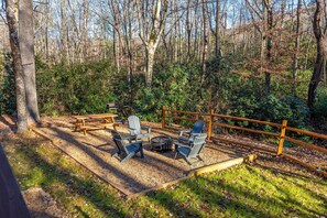 An outdoor seating area with Adirondack chairs and a fire pit, surrounded by a wooden fence and dense forest. - Hidden Hideaway 2 Bedroom Cabin by RedAwning (Cosby)