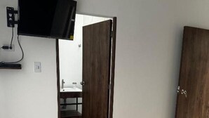 A room with a wooden wardrobe, a television mounted on the wall, and a bathroom visible through an open door. - Cozy 3-bedroom condo in enchanting Santa Rosa de Cabal with WiFi (Santa Rosa de Cabal)
