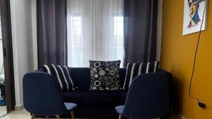 A living room with a dark blue sofa, two matching armchairs, a patterned throw pillow, and a large window with curtains. - Cozy 3-bedroom condo in enchanting Santa Rosa de Cabal with WiFi (Santa Rosa de Cabal)