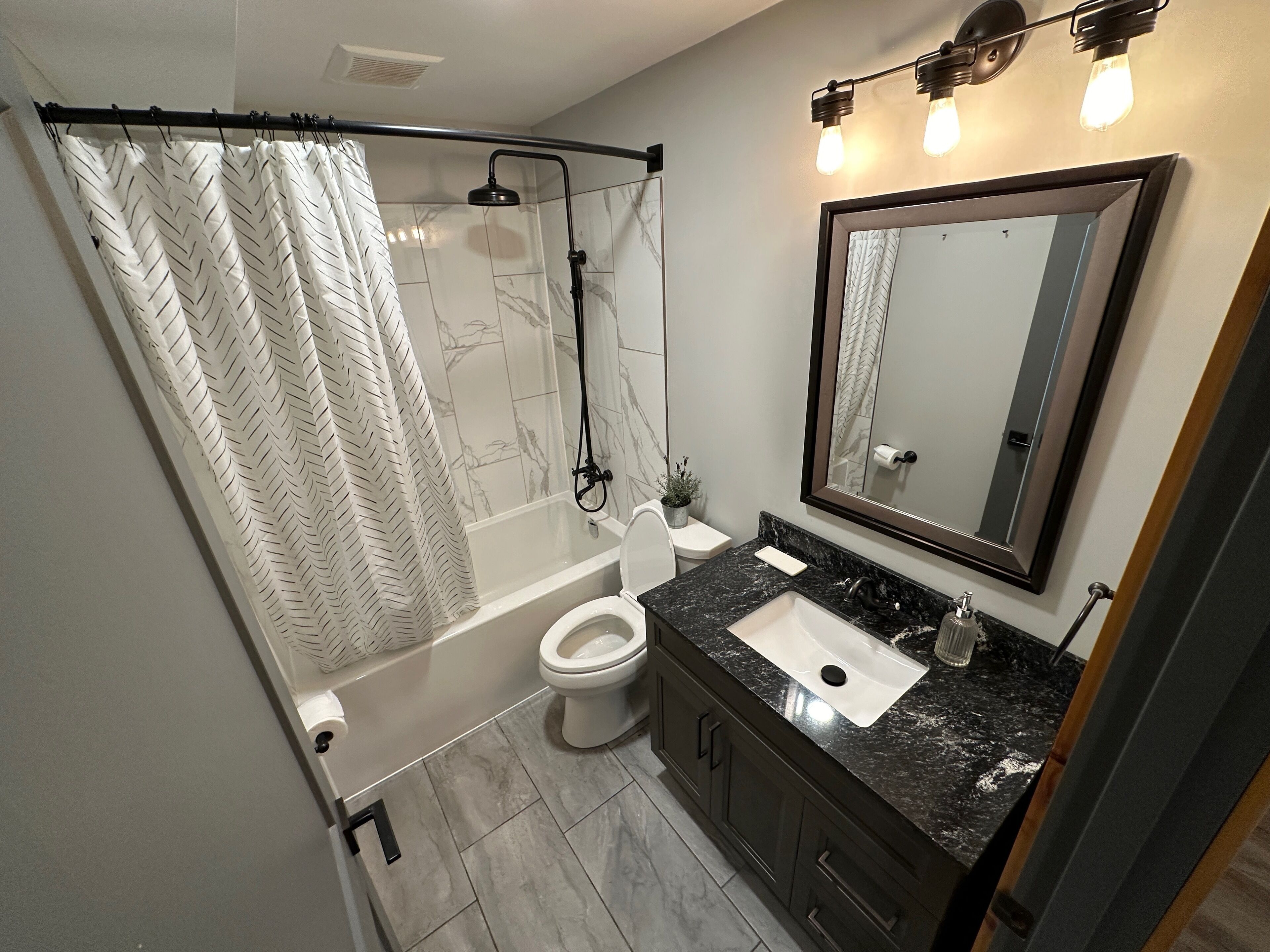 A bathroom with a shower, toilet, sink, and a large mirror.