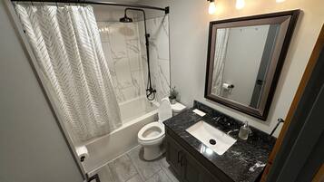 A bathroom with a shower, toilet, sink, and a large mirror.