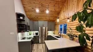 A modern kitchen with a stainless steel refrigerator, grey cabinets, and a wooden ceiling. - Waterfront Log Home with Beach and Hot Tub. Pet Friendly! (Clandeboye)