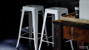 Une cuisine moderne dotée d’un grand îlot central, de tabourets de bar blancs, d’un luminaire suspendu et d’une plante en pot.