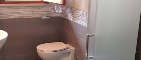 A small bathroom with two toilets, a sink, and a window.
