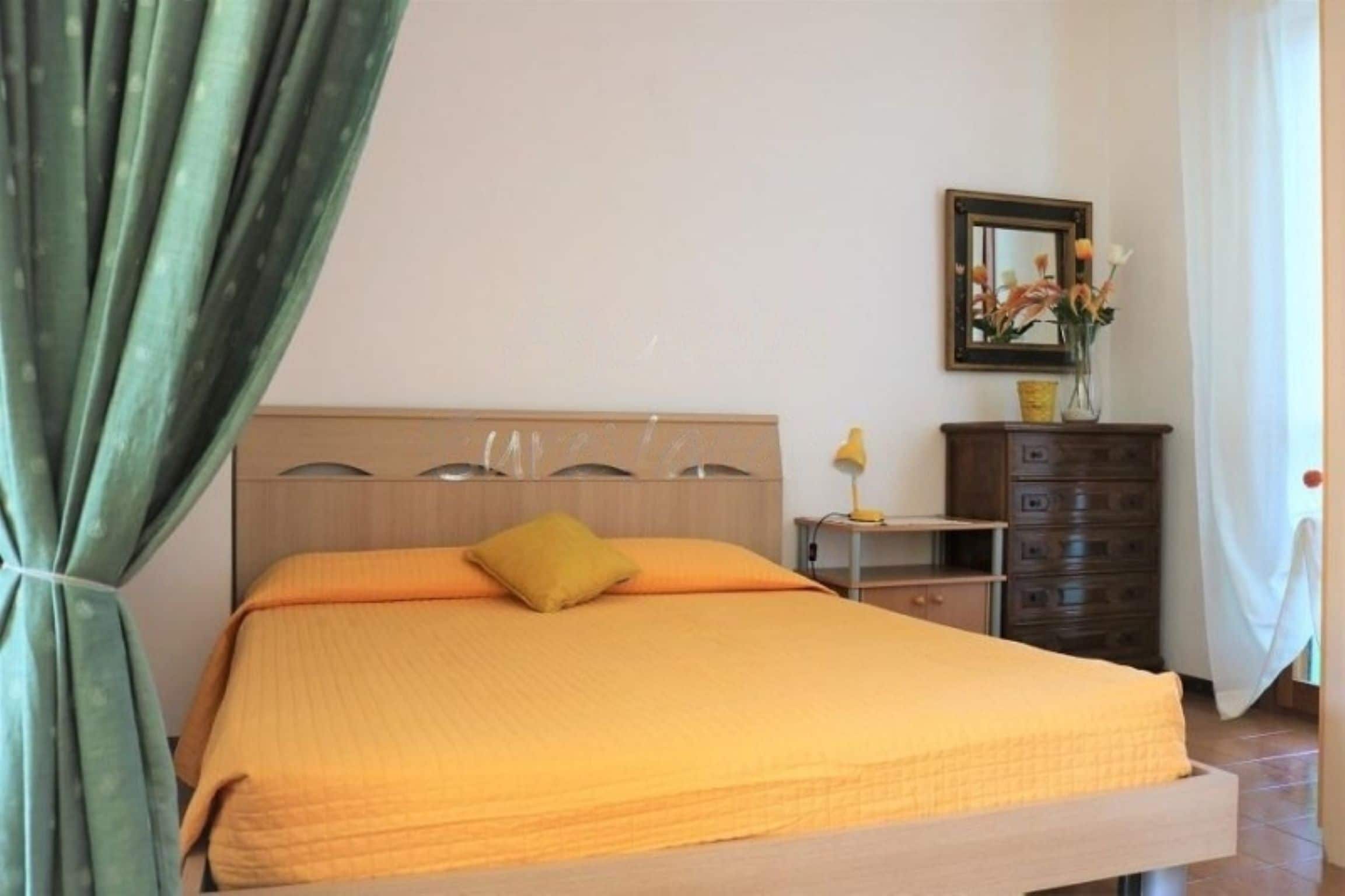 A bedroom with a bed, a nightstand, a dresser, and a mirror on the wall.