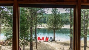 A cabin with a large window overlooking a lake, surrounded by trees. - Waterfront Loon Cottage | Private Boat Dock | Hot Tub (Island Park)