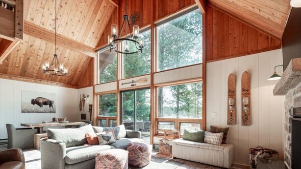 A spacious living room with a high ceiling, large windows, and a fireplace. - Waterfront Loon Cottage | Private Boat Dock | Hot Tub (Island Park)