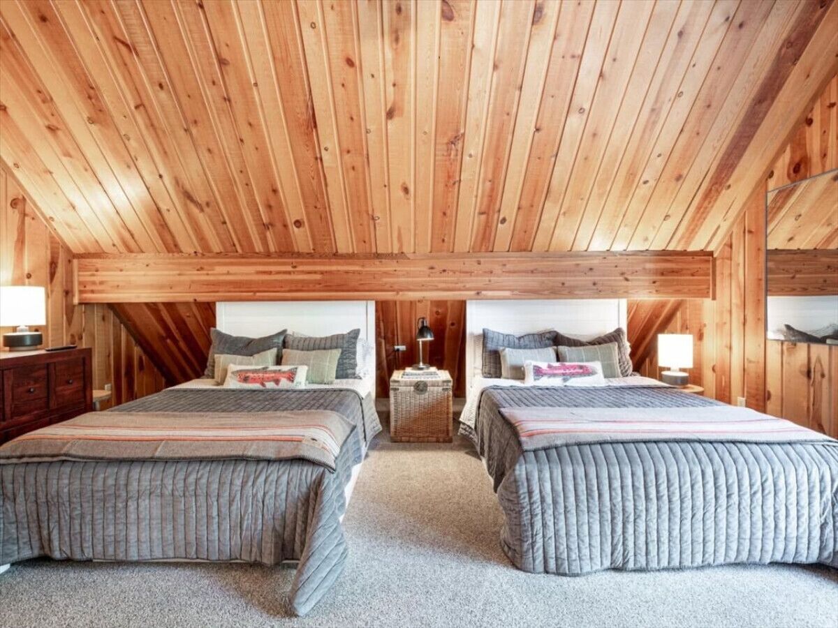 Une chambre confortable située sous les toits, avec deux lits, des poutres en bois au plafond et une petite table avec une lampe.