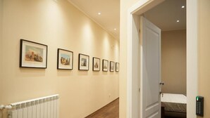 A hallway with framed pictures on the wall, a radiator, and a door leading to a room with a bed. - Miramare Luxury Suites (Trieste)