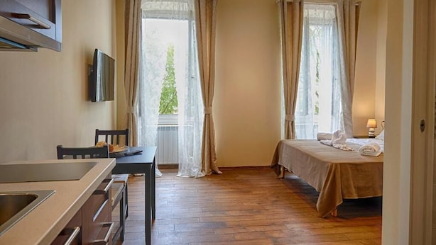 A hotel room with a bed, a desk, a TV, and large windows with curtains. - Miramare Luxury Suites (Trieste)