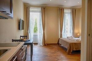 Habitación de hotel con cama, escritorio, televisor y ventanas amplias con cortinas.