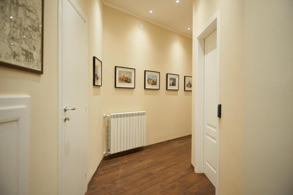 A hallway with a radiator, wooden flooring, and framed pictures on the wall.