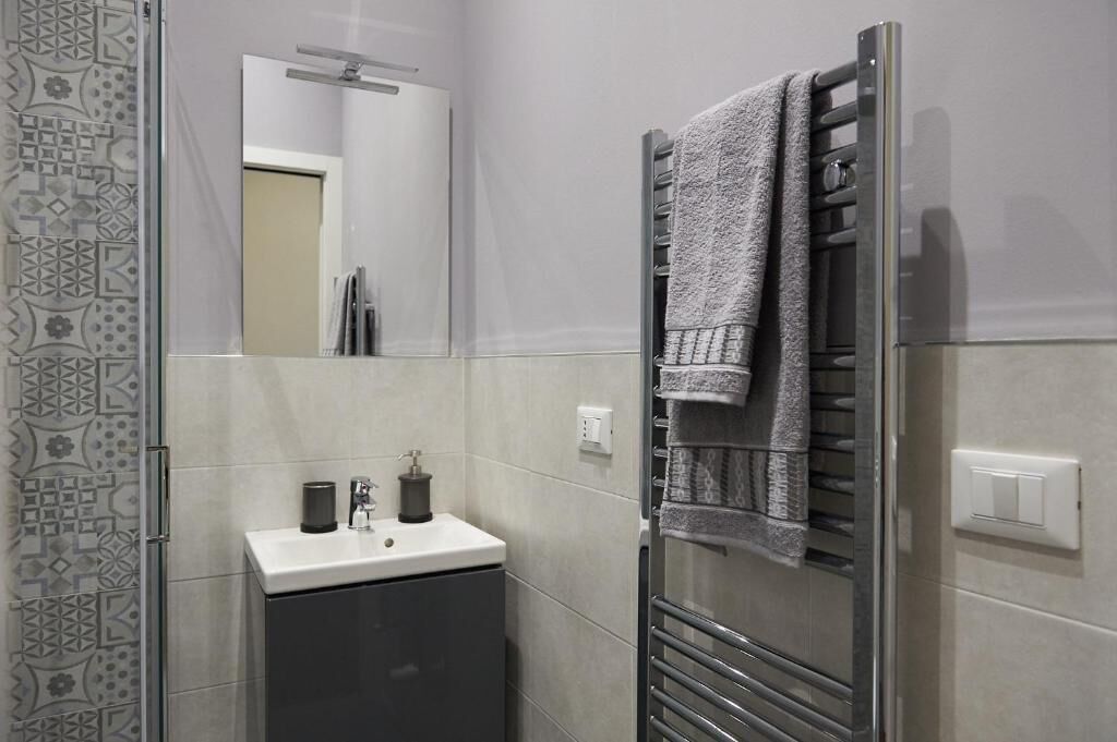 Une salle de bain moderne avec une douche à parois de verre, un lavabo blanc avec un meuble sombre et un porte-serviettes avec une serviette.