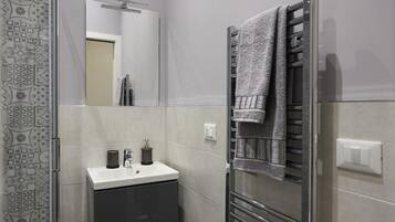 Une salle de bain moderne avec une douche à parois de verre, un lavabo blanc avec un meuble sombre et un porte-serviettes avec une serviette.