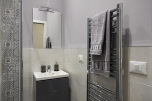 A modern bathroom with a glass shower enclosure, a white sink with a dark cabinet, and a towel rack with a towel. - Miramare Luxury Suites (Trieste)