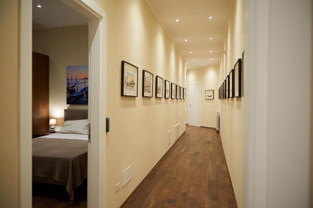 Ein Hotelgang mit gerahmten Kunstwerken an den Wänden, einem Bett mit Kopfteil und einem Holzboden.