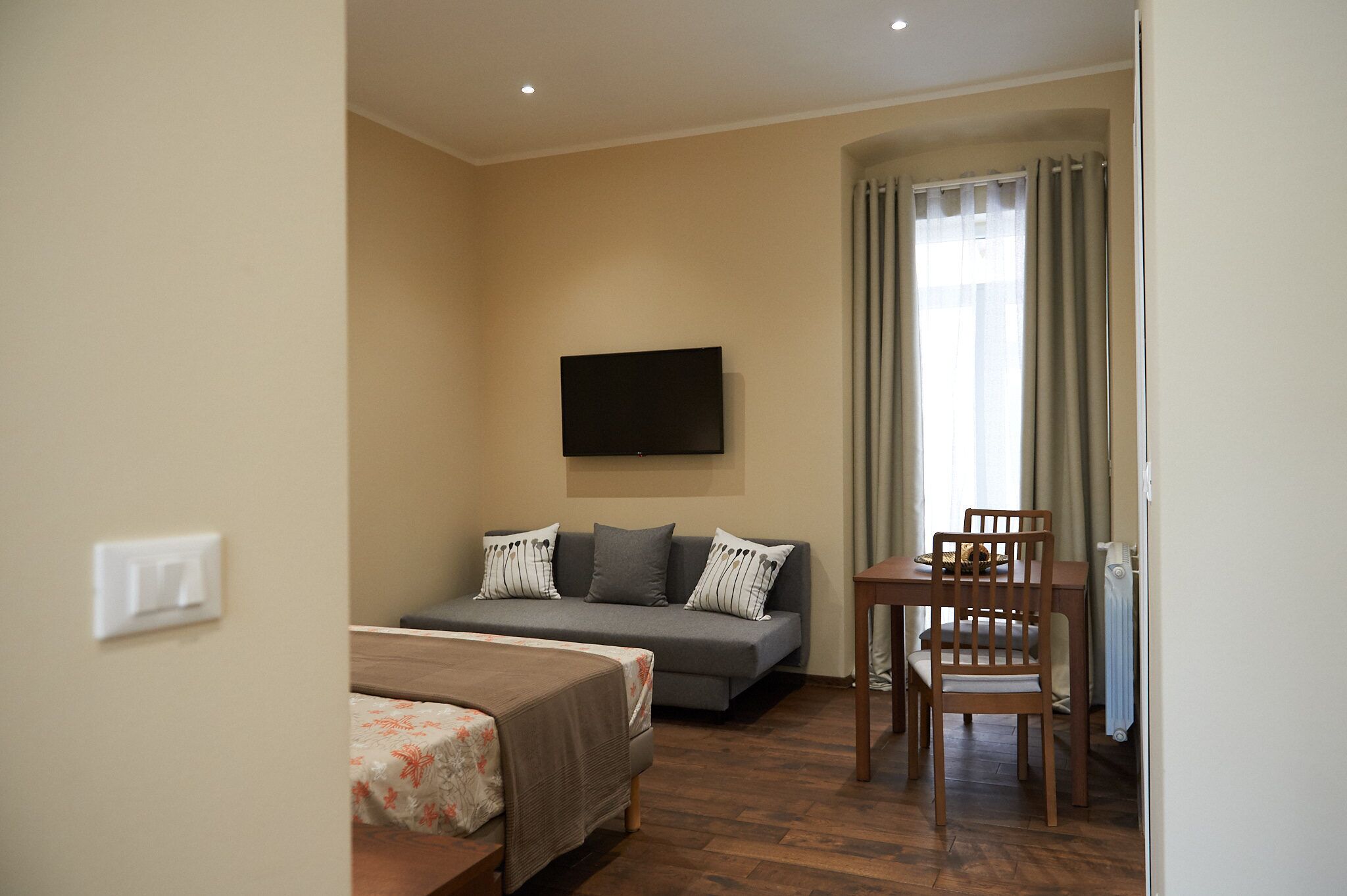 Hotelkamer met een bank, een bed, een tafel met stoelen en een aan de muur bevestigde televisie.