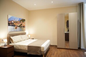 A bedroom with a bed, bedside tables, a wardrobe, and a painting of a coastal town. - Miramare Luxury Suites (Trieste)