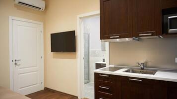 A compact kitchen with wooden cabinets, a stainless steel sink, and a flat-screen TV mounted on the wall.