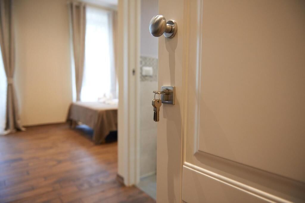 Een deur met een sleutelgat en slot, leidend naar een kamer met een bed en een raam.