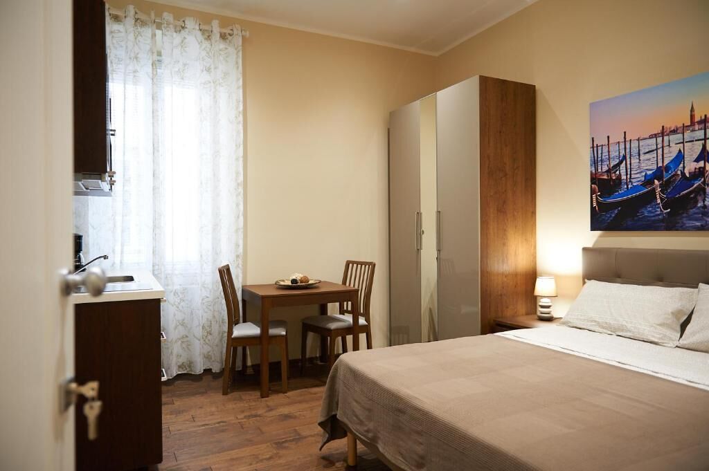 Habitación de hotel con cama, escritorio y silla, una mesita con un plato de comida, armario y un cuadro que representa una escena de un canal.