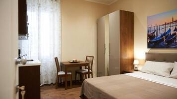 Habitación de hotel con cama, escritorio y silla, una mesita con un plato de comida, armario y un cuadro que representa una escena de un canal.