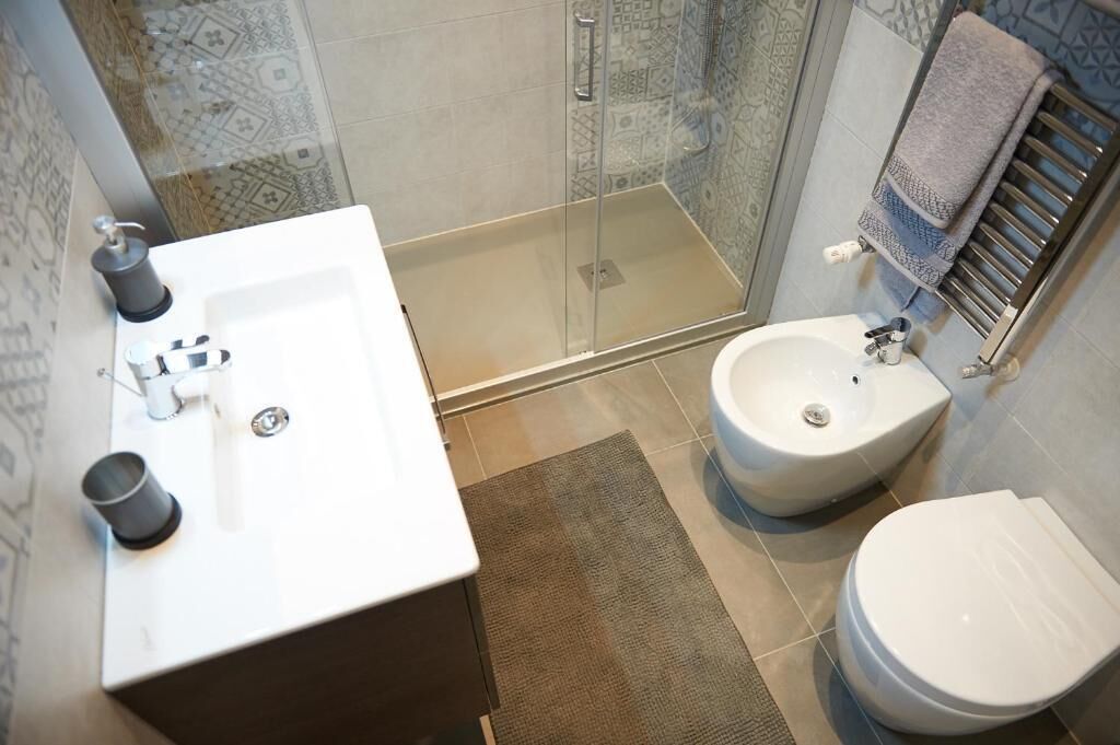 A bathroom with a glass shower enclosure, a white sink, a bidet, and a toilet.