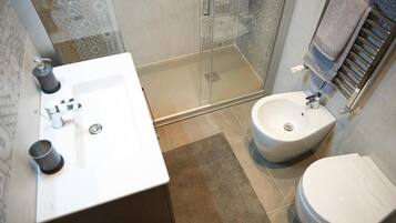 A bathroom with a glass shower enclosure, a white sink, a bidet, and a toilet.