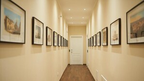 A hallway with framed pictures on the walls, a wooden floor, and a white door at the end. - Miramare Luxury Suites (Trieste)