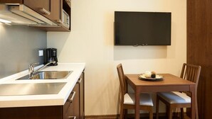 A compact kitchen with a built-in stove, a coffee maker, and a dining area with a TV mounted on the wall. - Miramare Luxury Suites (Trieste)