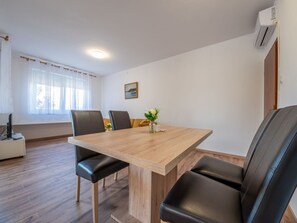 Zona menjador moderna amb taula de fusta i cadires de cuir negre. Hi ha un finestral amb cortines transparents, un quadre a la paret i un aparell d'aire condicionat fixat a la paret.