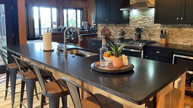 A modern kitchen with dark cabinetry, a large island, and a stone backsplash.