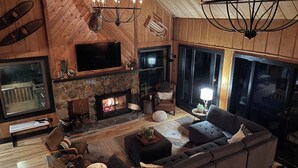 A cozy living room with a stone fireplace, a large flat-screen TV, a sectional sofa, and a chandelier.