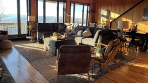 A spacious living room with a large sectional sofa, a wooden dining table, and a view of the mountains through large windows.