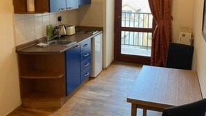 A compact kitchen with a wooden table and chairs, a built-in oven, and a window with curtains.