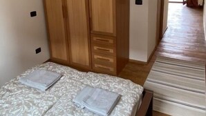 A bedroom with a bed, a wooden wardrobe, and a view of the outside.