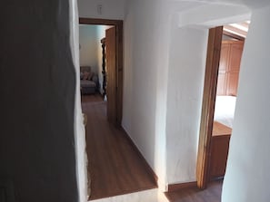 A narrow hallway with wooden flooring and white walls, leading to a room with a bed and wooden furniture.