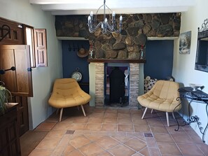 A cozy room with a stone fireplace, two armchairs, a clock, and a wooden door.