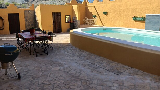 Une terrasse avec une piscine, un revêtement de sol en pierre, un barbecue et du mobilier d’extérieur.