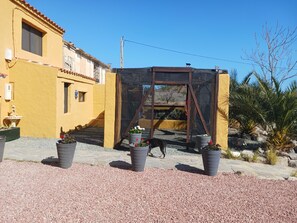 A yellow building with a window and a door, surrounded by gravel and potted plants.