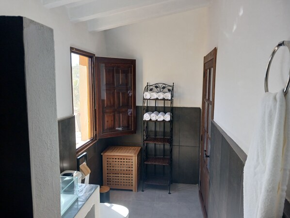 Une petite salle de bain avec une porte en bois, un porte-serviettes en métal, un tabouret en bois et une cloison en verre.